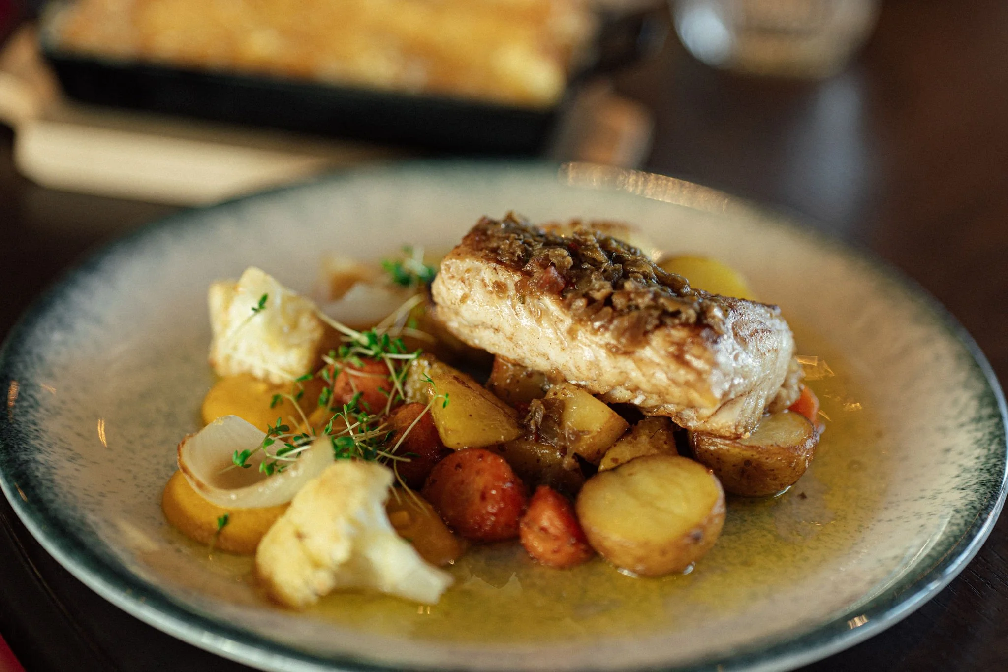 En tallerken med en stekt fiskefilet med sitron, servert med poteter, gulrøtter, blomkål og urter.