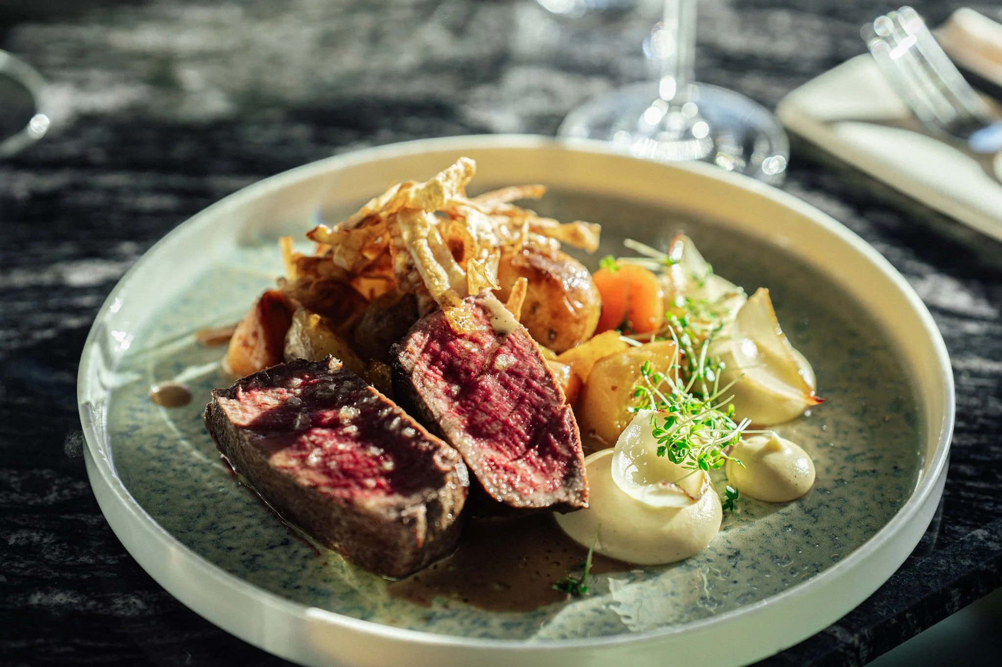Tynnskåret oksestek med rosa midt og brun skorpe, servert med poteter og grønnsaker, på en tallerken med saus og garnityr.