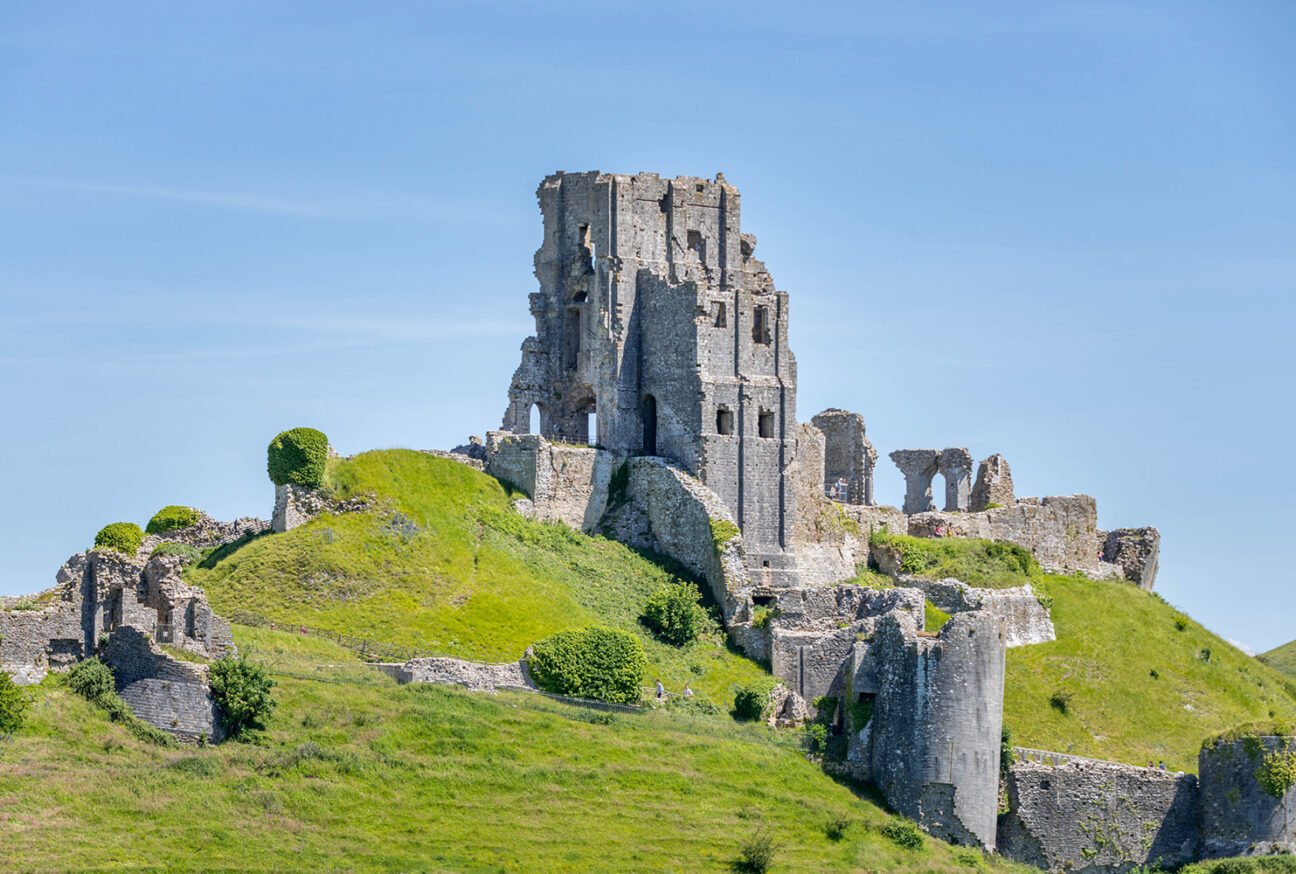 Ruins of a castle on a grassy hill under a blue sky.