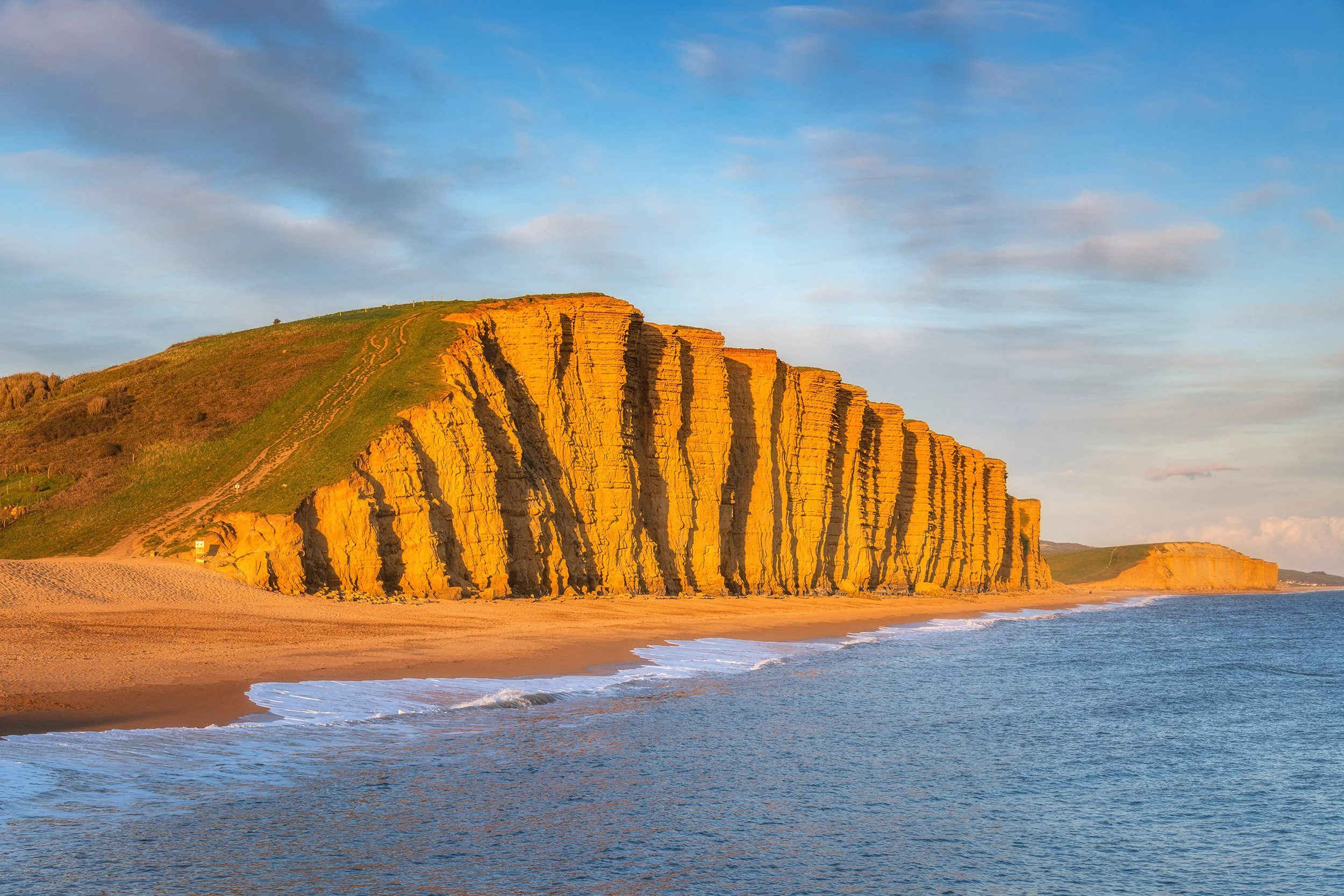 Cliffs along a beach during sunset with a partly cloudy sky.