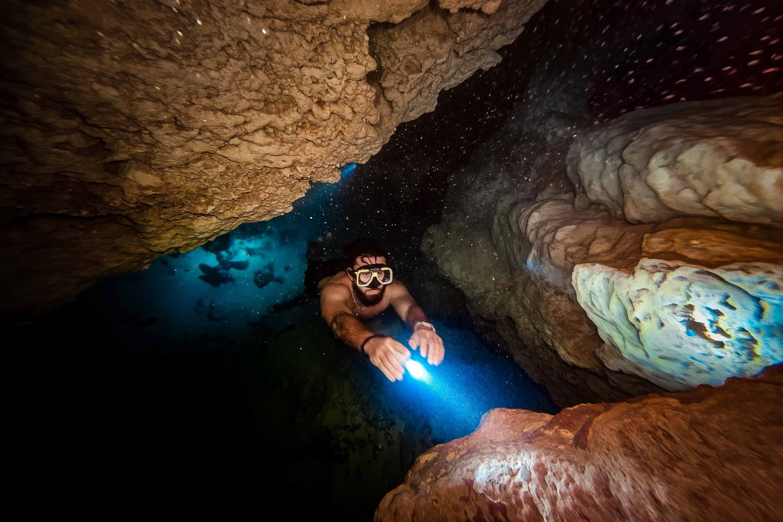 A person in snorkeling gear exploring inside a narrow underwater cave with rocky walls and a blue light.