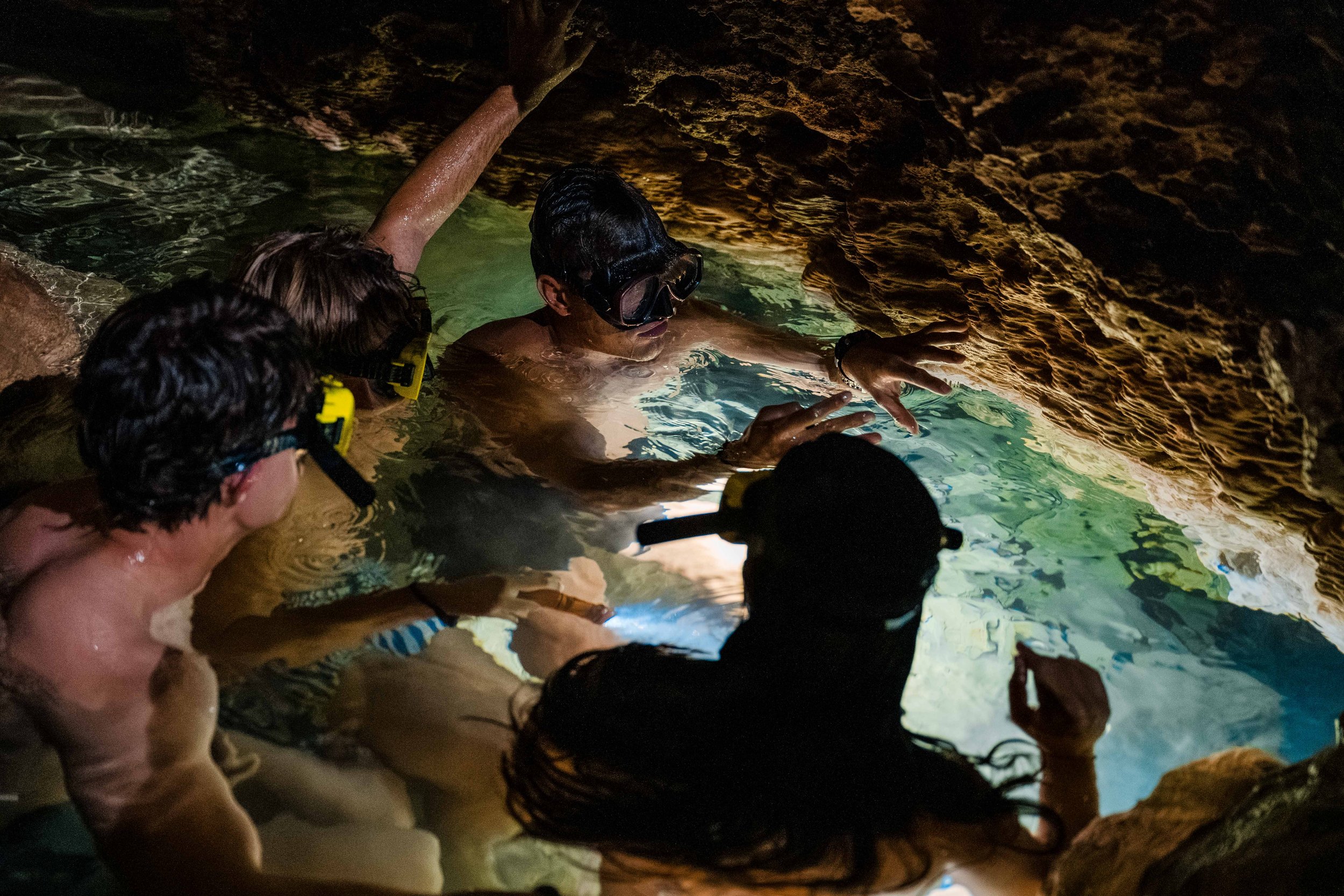 Group of people wearing snorkeling masks and swimming in a cave with rocky walls.