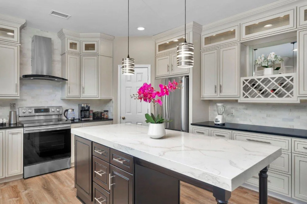 Modern kitchen with white cabinets, a large marble island, stainless steel appliances, and pendant lights. There's a potted pink orchid on the island.