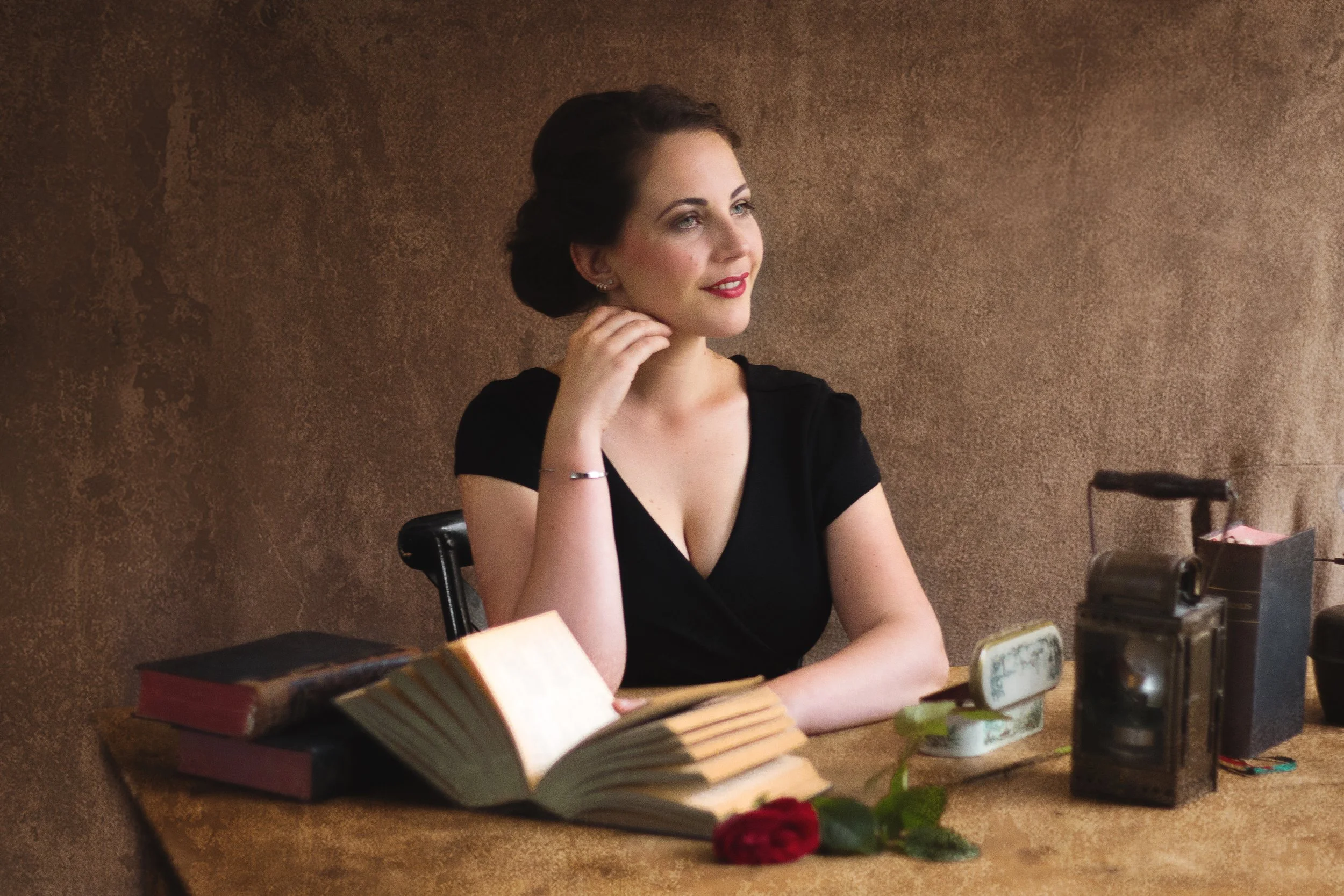 Tineke Roseboom zit aan een tafel met boeken en een lantaarn, voor een bruine achtergrond.
