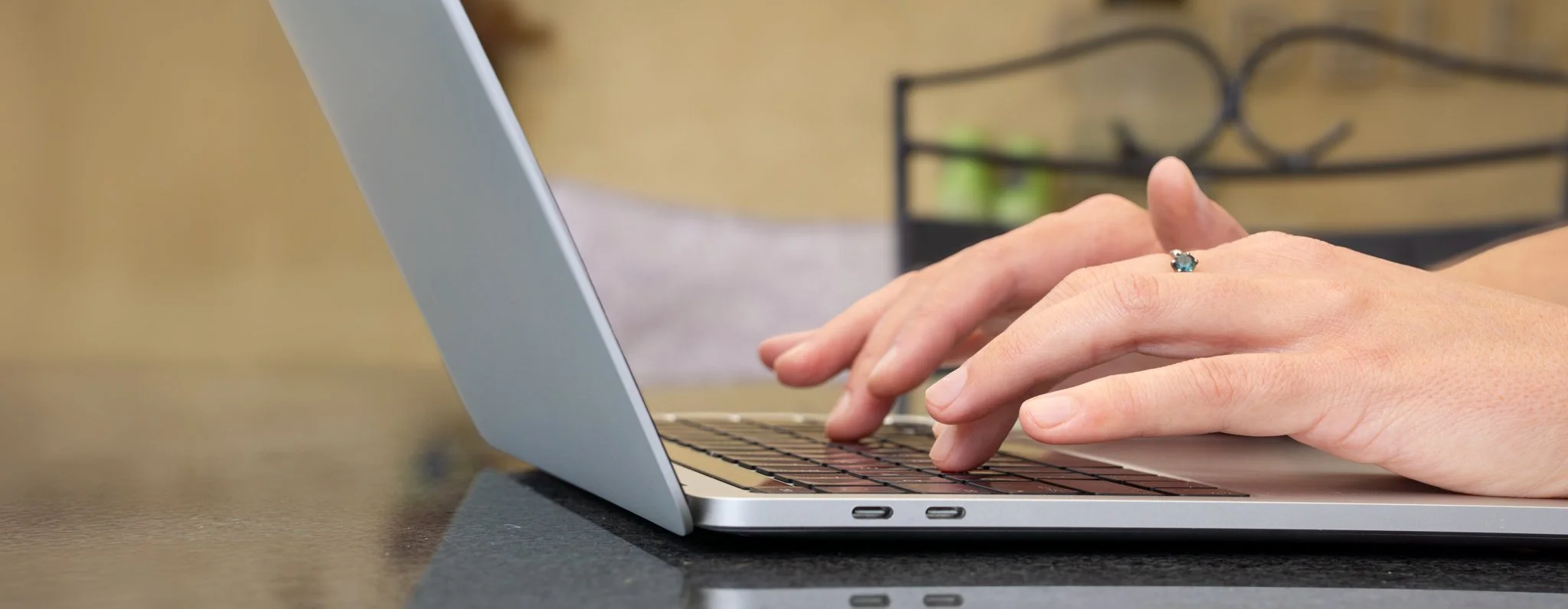 Close-up of a person typing on a laptop at a desk while wearing a ring.