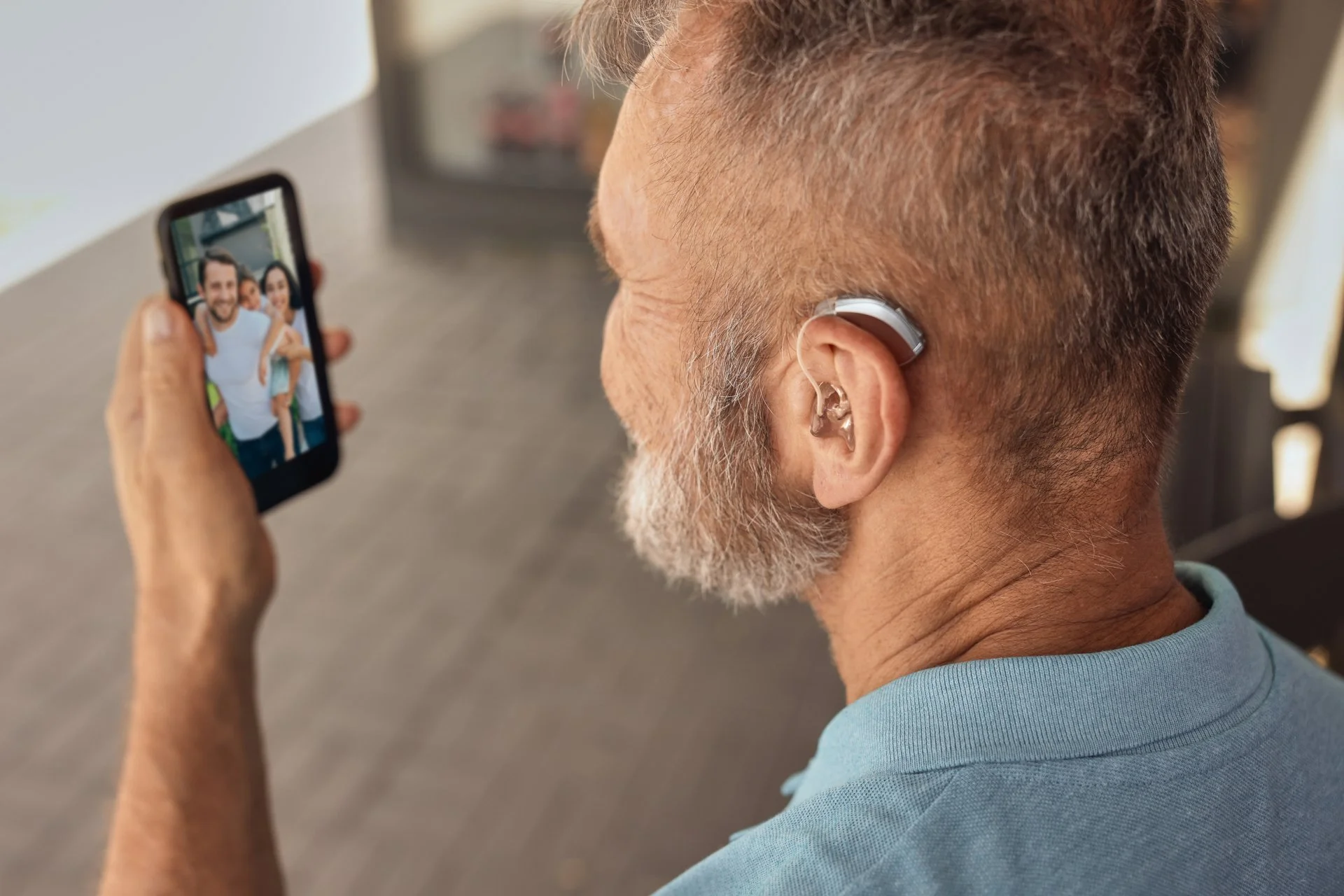 Older man wearing a hearing aid looks at a family photo on his smartphone