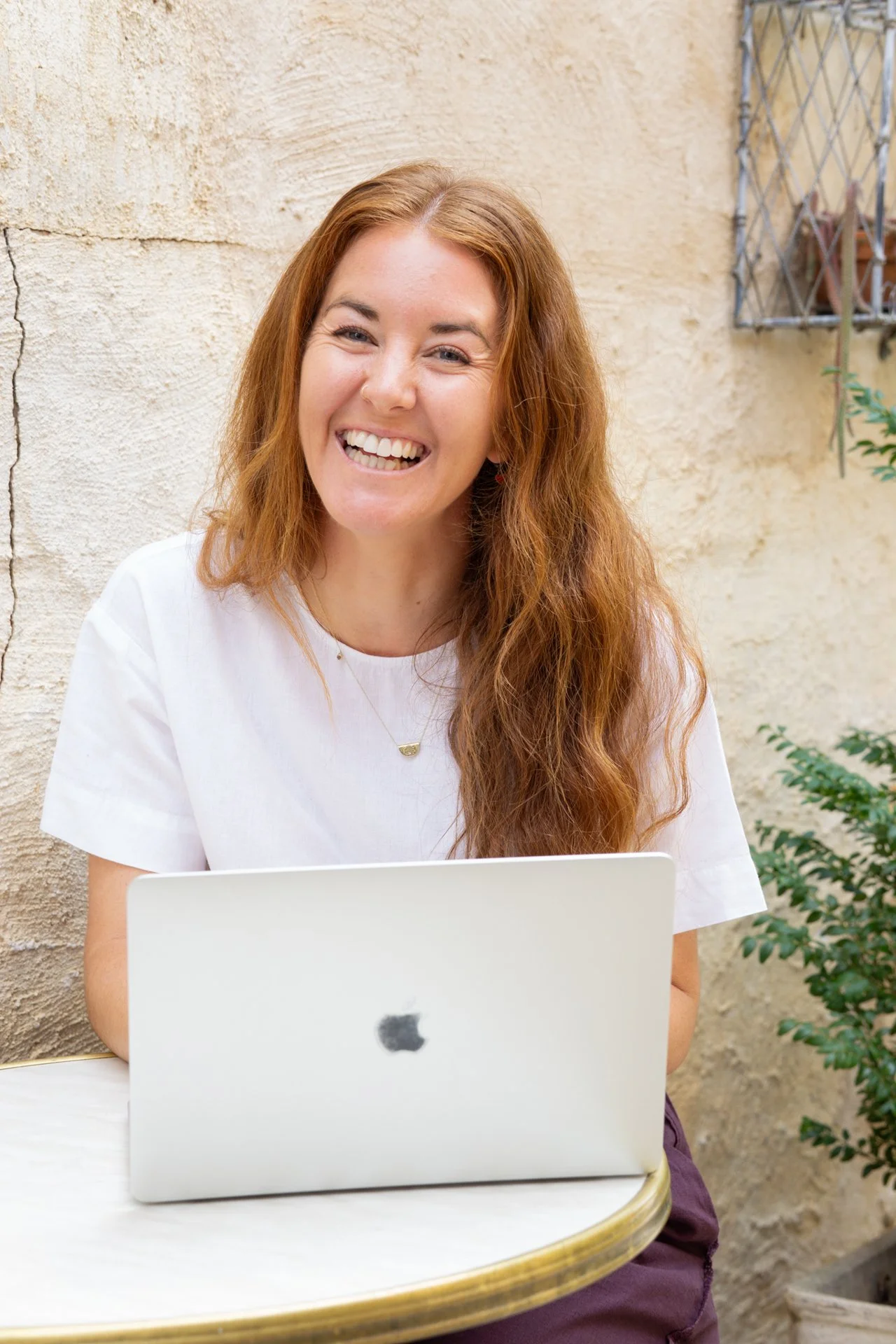 Smiling woman with long red hair using a MacBook laptop outdoors