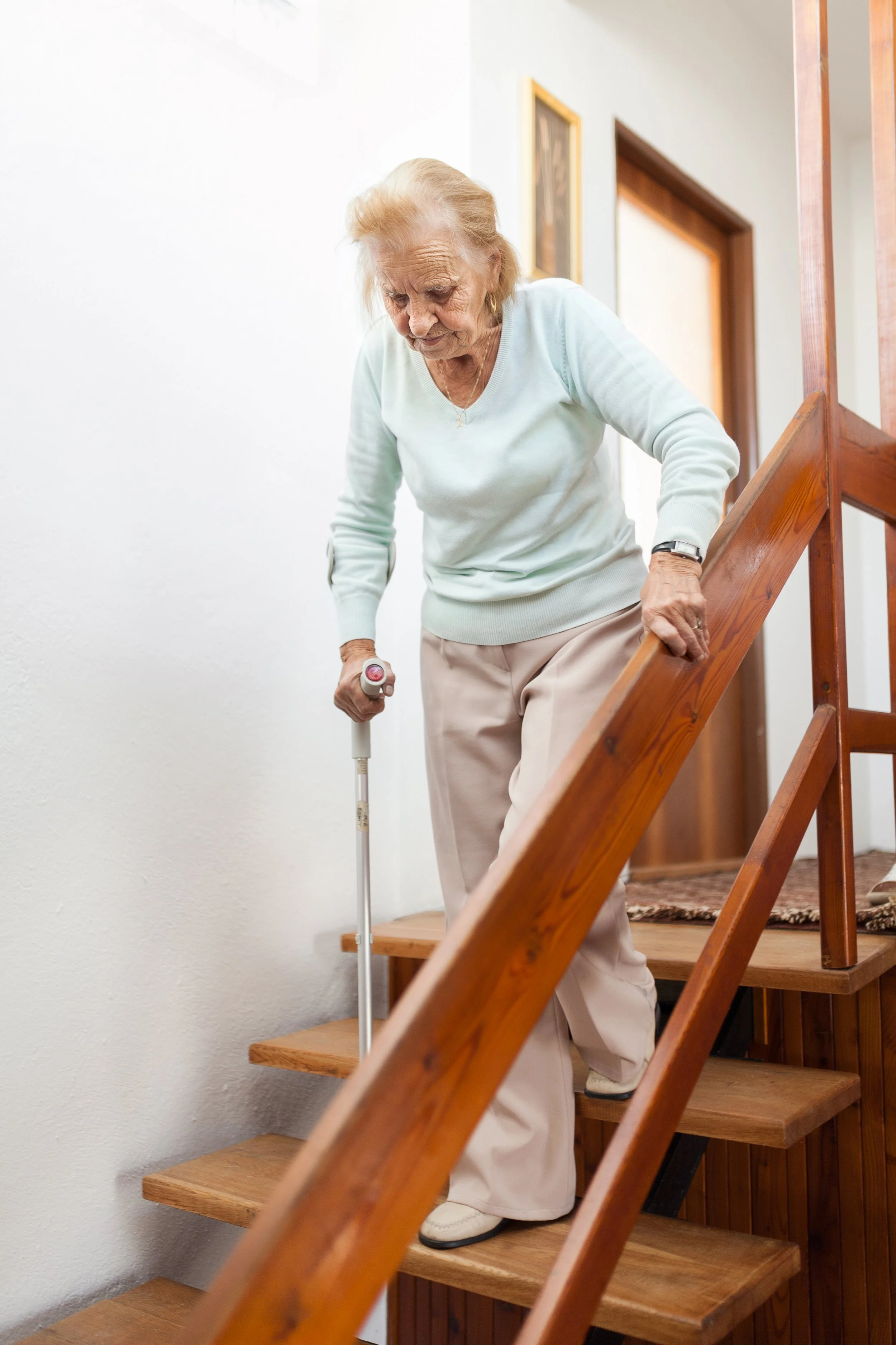 Elderly woman using a cane while climbing indoor wooden stairs
