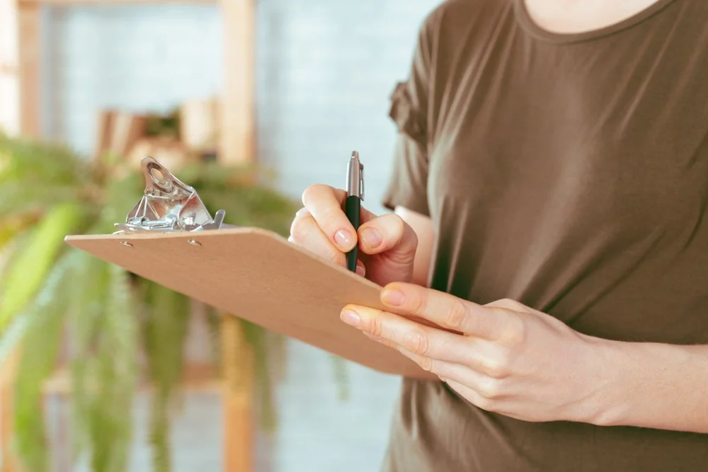 Person writing on a clipboard with a pen indoors