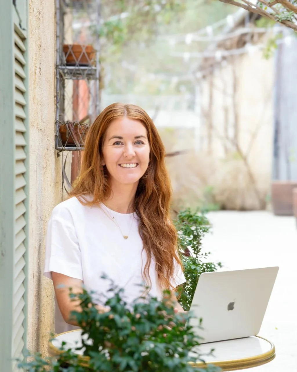 Smiling woman working on a laptop at an outdoor café table