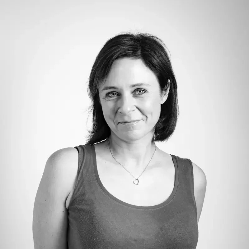 Black and white portrait of a woman with shoulder-length hair, smiling softly at the camera, wearing a sleeveless top and a necklace with a heart pendant.
