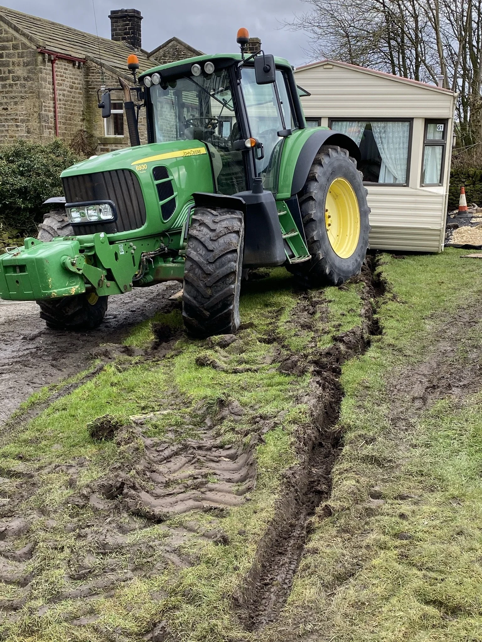 A green John Deere tractor with a large trench dug into the ground.
