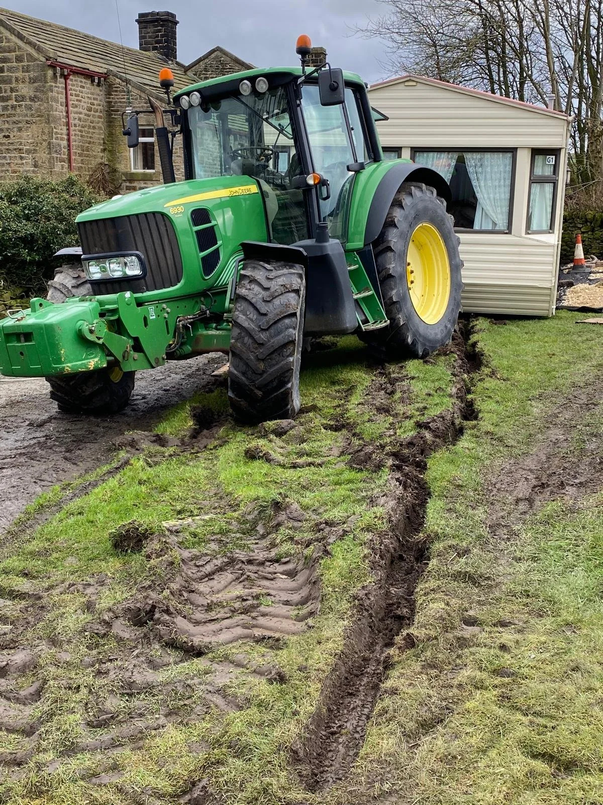 A green John Deere tractor with deep tire tracks and a trench in the grass.