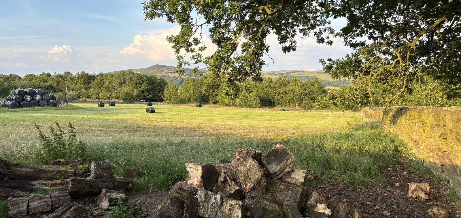 View across the fields at Blue Cuckoo Farm in Addingham, West Yorkshire, with hay bales, trees and the surrounding hills