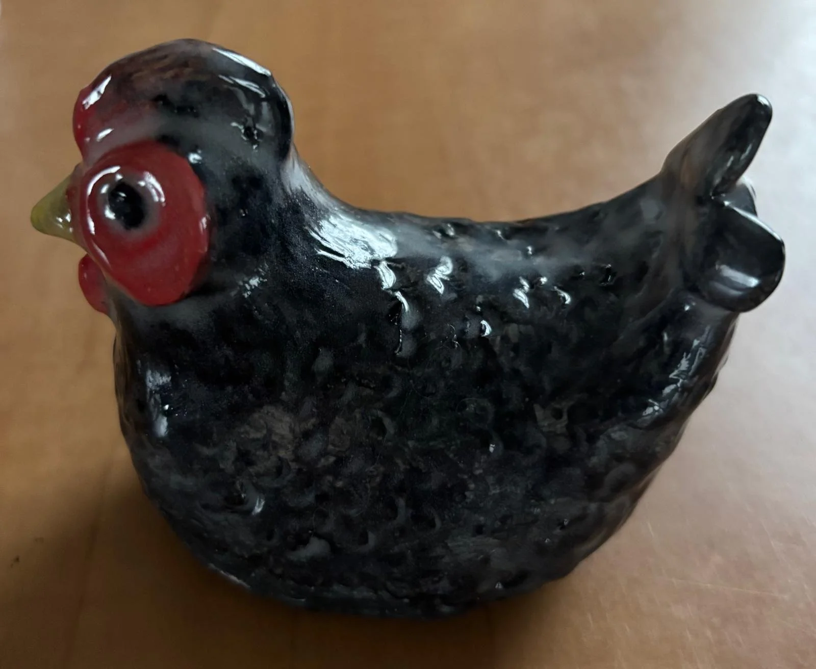 Ceramic figurine of a black chicken with a red face and a yellow beak, viewed from an angle.
