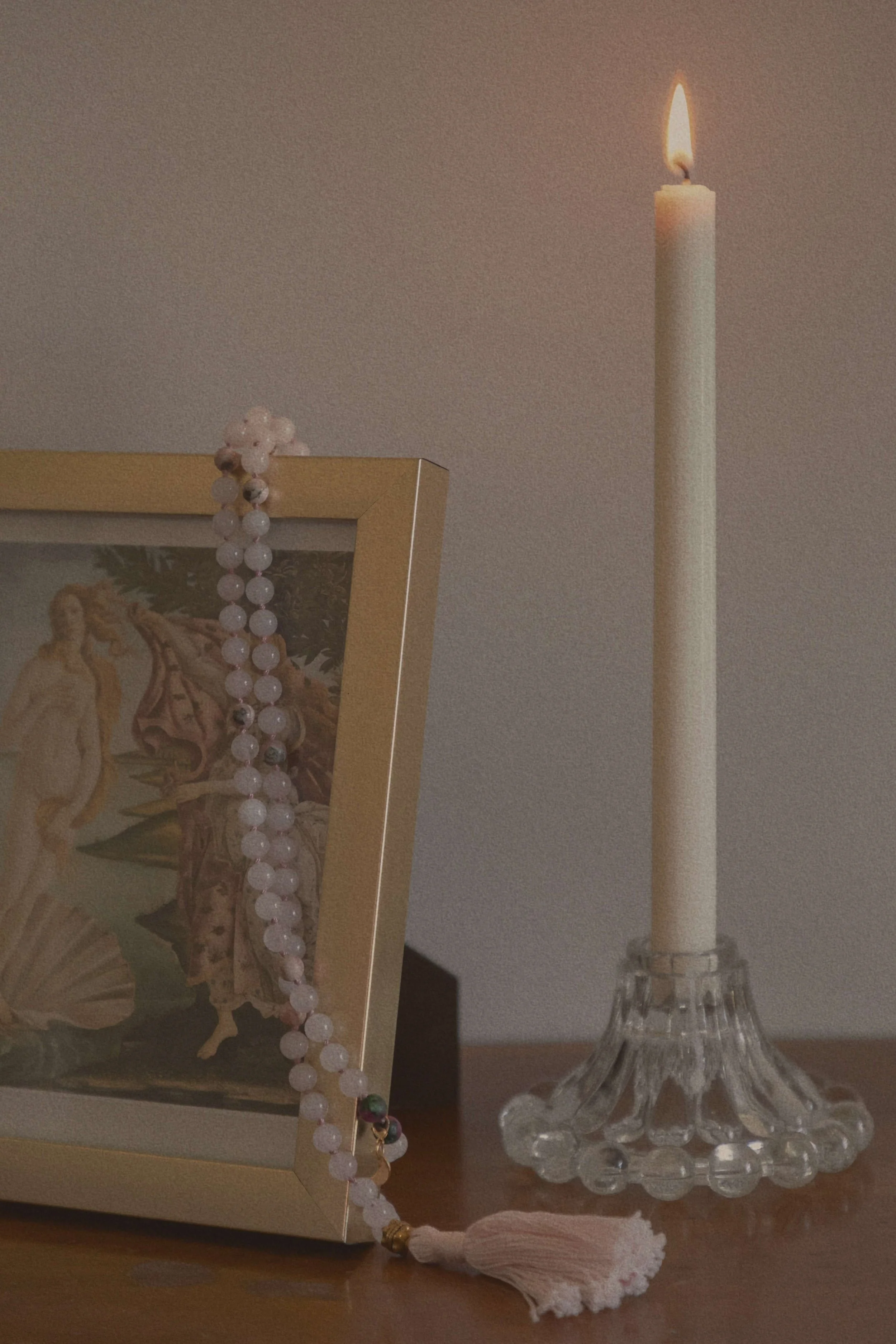 gold framed picture of venue and her shell with a string of rose quartz mala beads and a lit candle