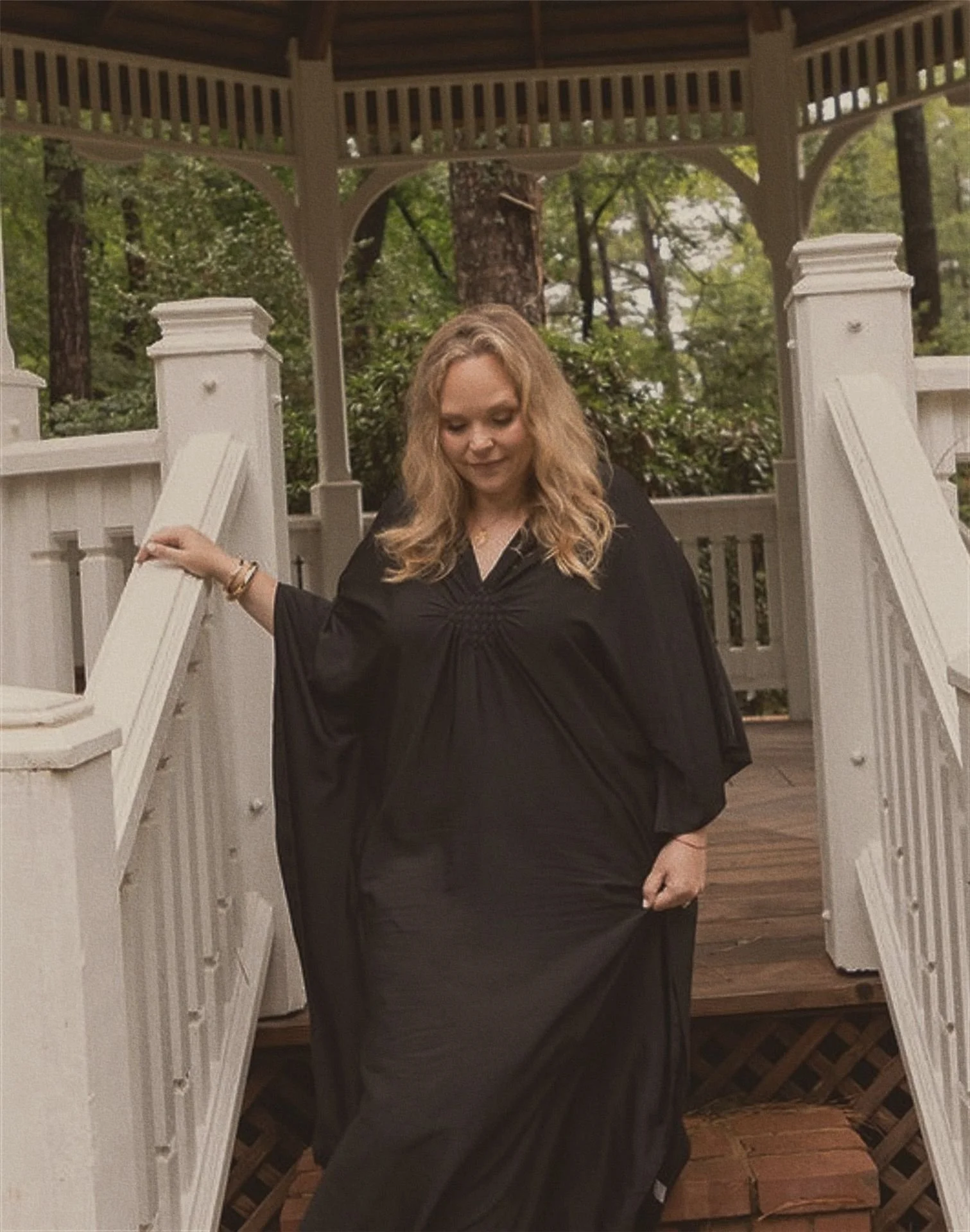 A woman in a black dress standing on a wooden porch with white railing and gazebo.