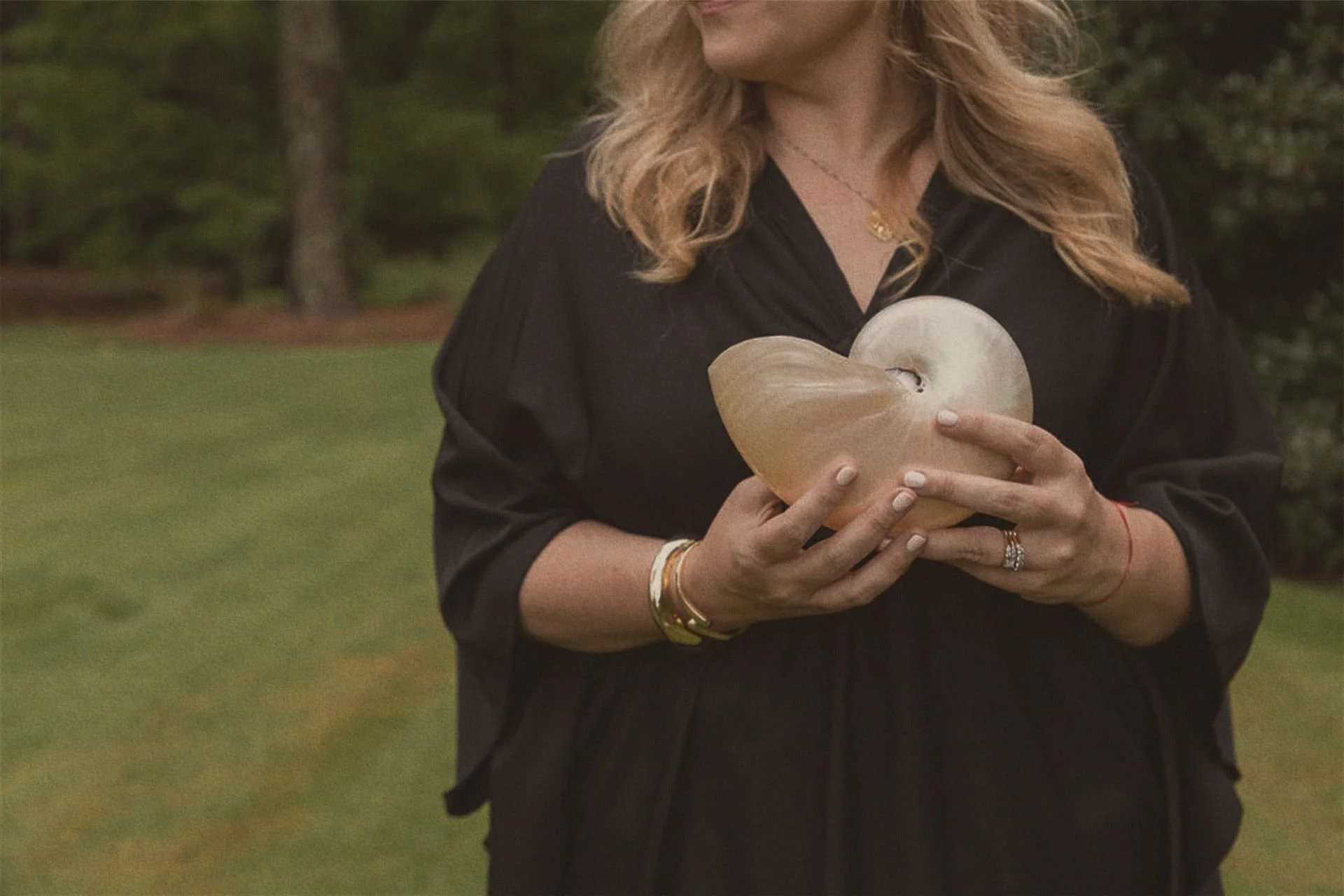 Danielle Hendrickson, Venusian astrologer, holding a heart-shaped seashell in a garden