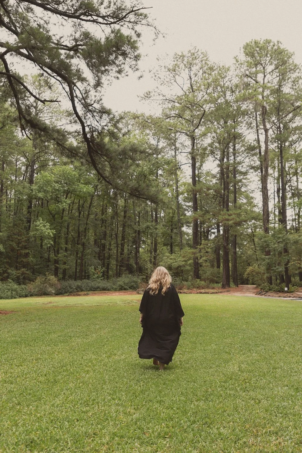 Danielle Hendrickson walking through a tree-lined meadow in a flowing black gown, walking with Venus