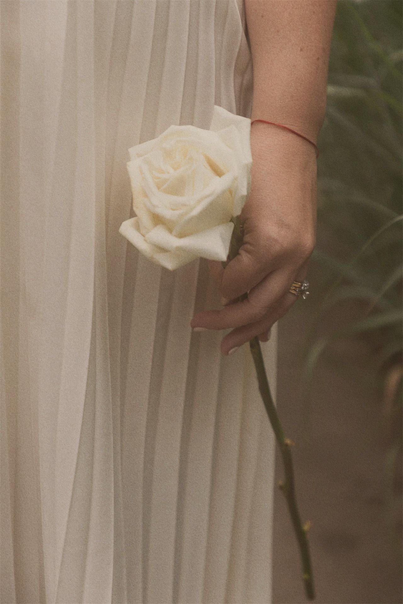 Woman in a flowing cream pleated gown holding a single white rose, embodying the Sacred Feminine