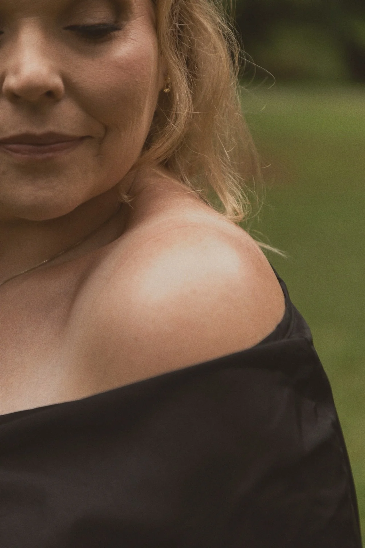 Danielle Hendrickson, Priestess of the Rose Lineage, in a black off-shoulder dress with eyes lowered in a garden