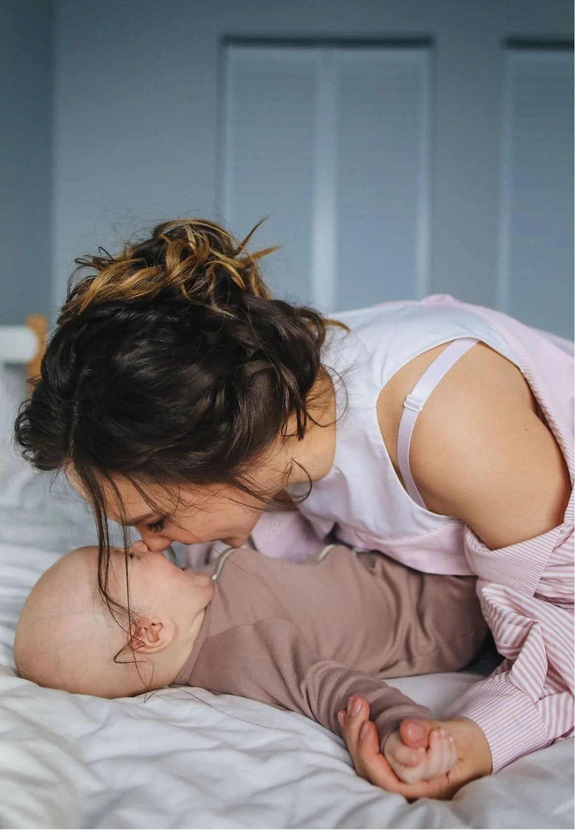 Mother kissing her baby while cuddling together on a bed