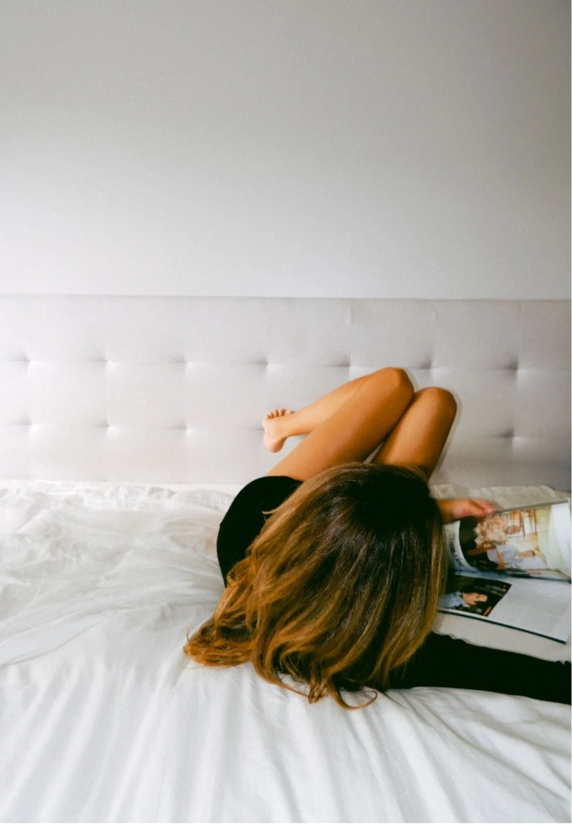 Woman lying on a white bed reading a magazine