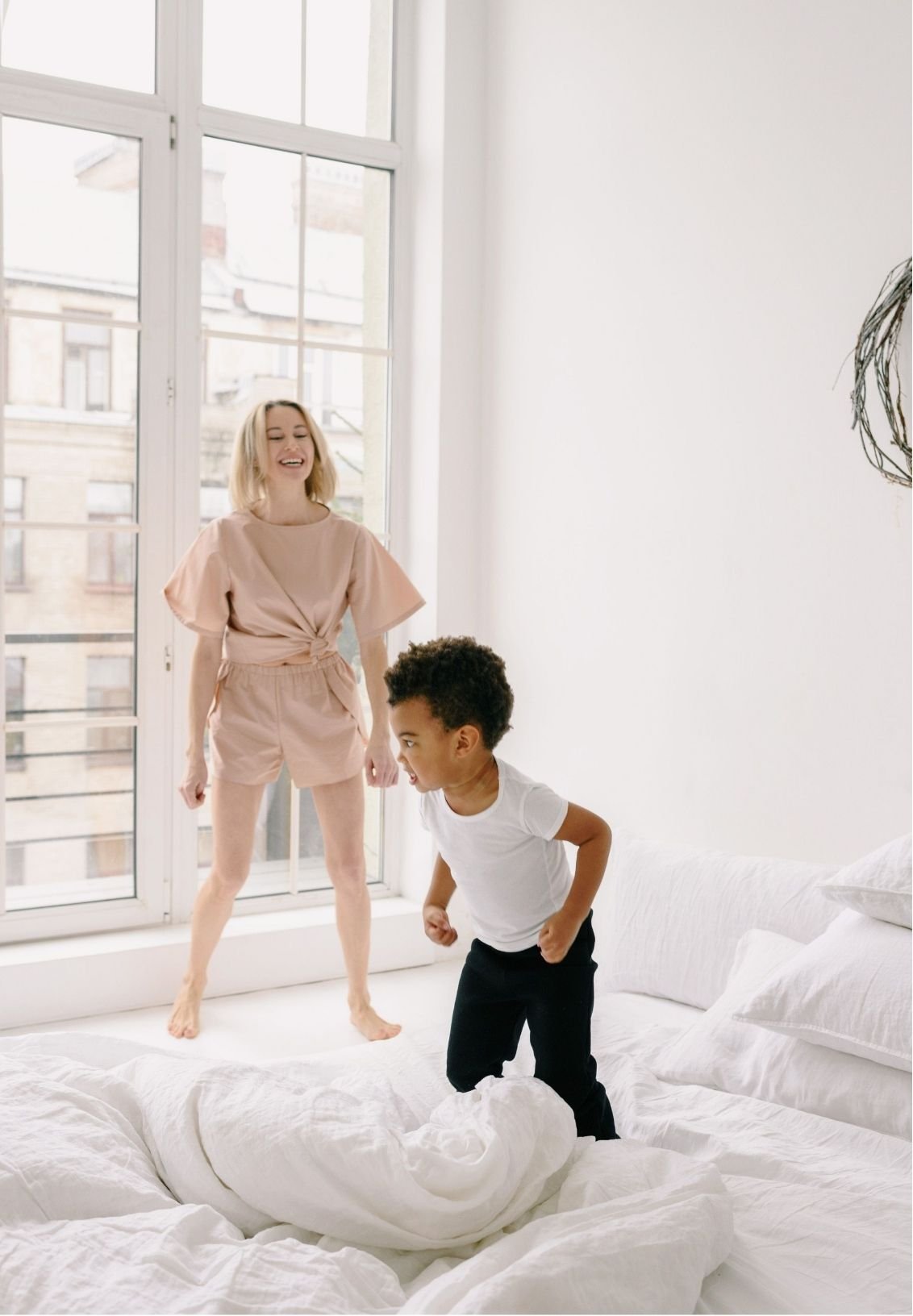 Mother and young son playing on a white bed in a bright bedroom