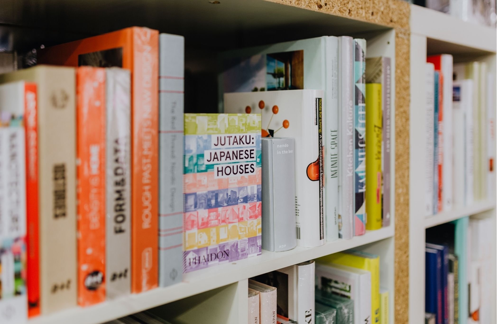 Colorful architecture and design books arranged on a white bookshelf, including a book on Japanese houses.