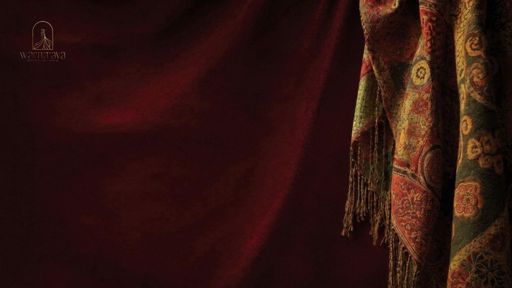 A dark, rich red background with a silk curtain displaying intricate floral and paisley patterns, partially draped to the right. The top left corner features a small, gold logo with a stylized figure and the text "Warnaraya" underneath.