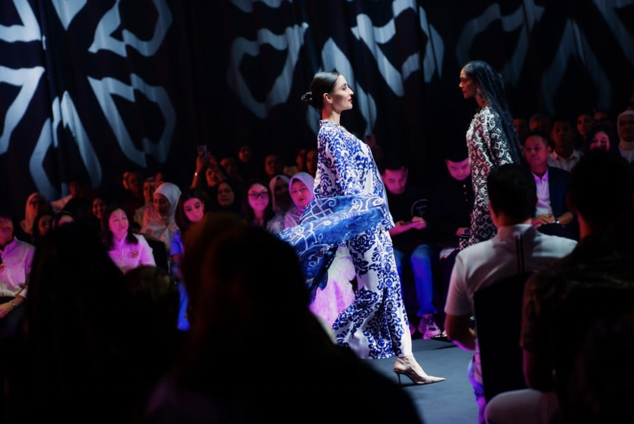 Models walking on a runway during a fashion show, with an audience watching.