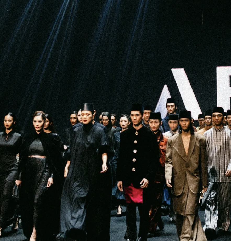 Group of models walking on runway at a fashion show, wearing traditional and modern clothing.
