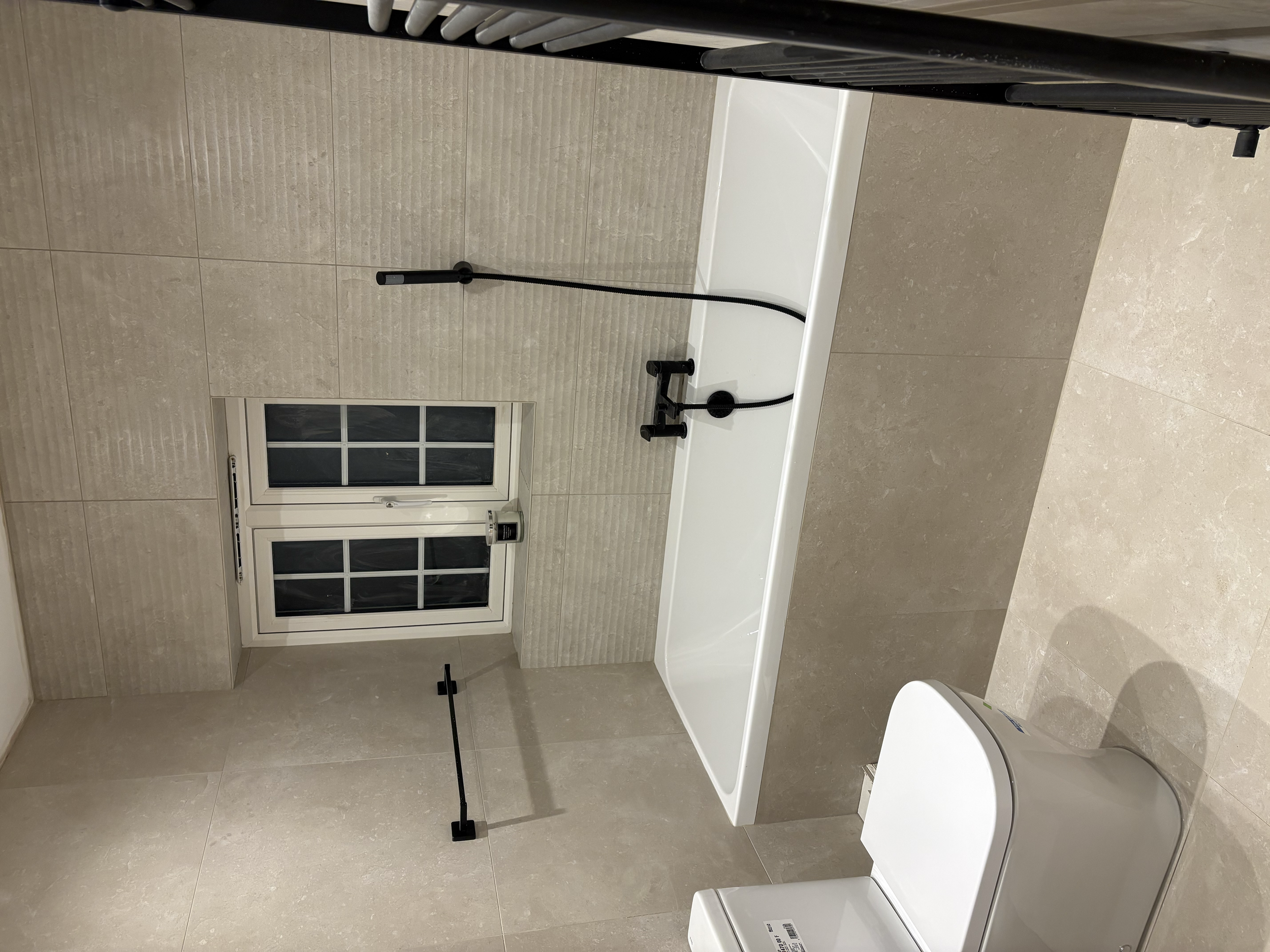 Bathroom with a bathtub, toilet, window, and beige tiled walls and floor.