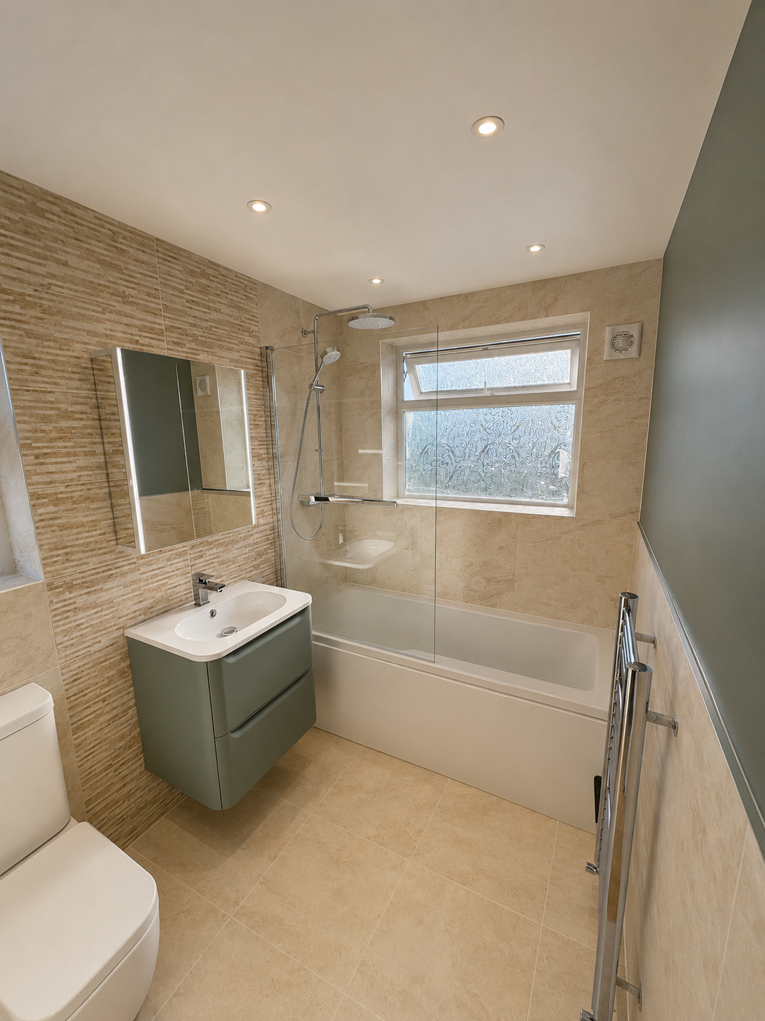 Modern bathroom with beige tiles, green accent wall, and a bathtub with a frosted window. Features include a mirror, sink with cabinet, and a heated towel rack.