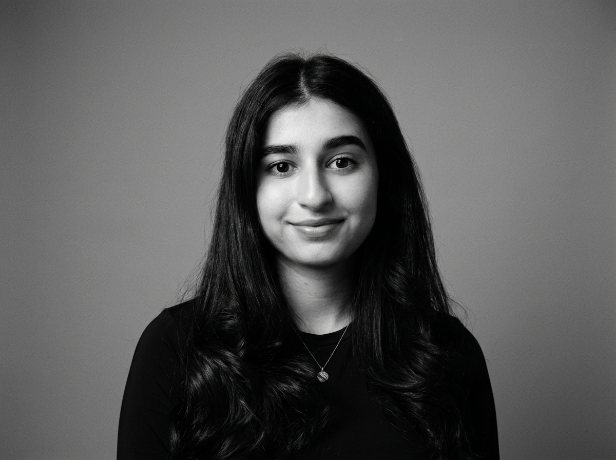 Black and white portrait of a young woman with long wavy hair wearing a dark top and a necklace, smiling gently, against a plain background.