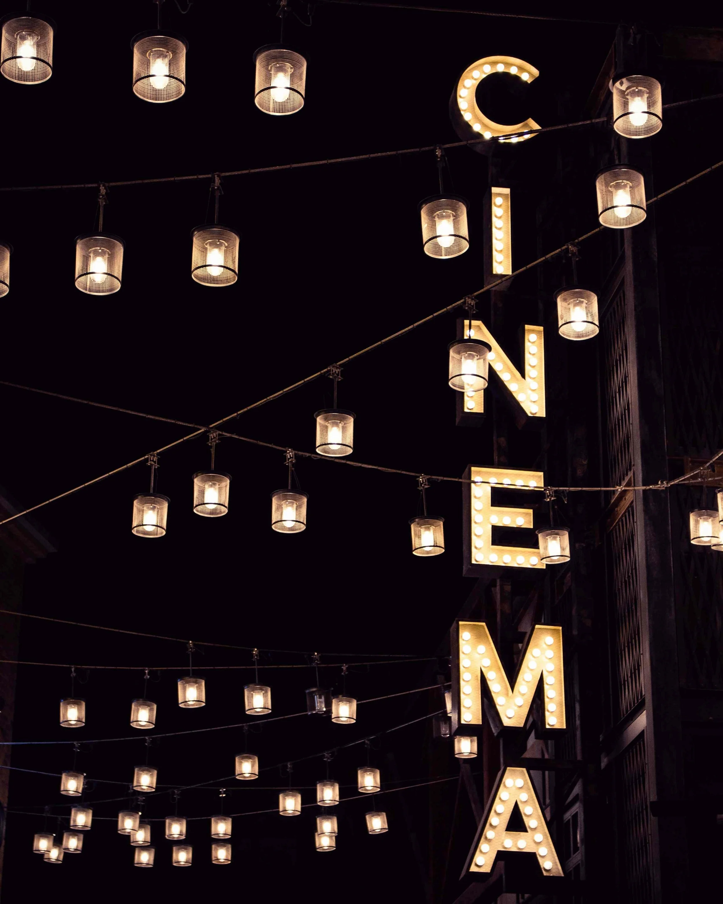 Night scene with lit string lights hanging overhead and illuminated marquee letter 'C'.