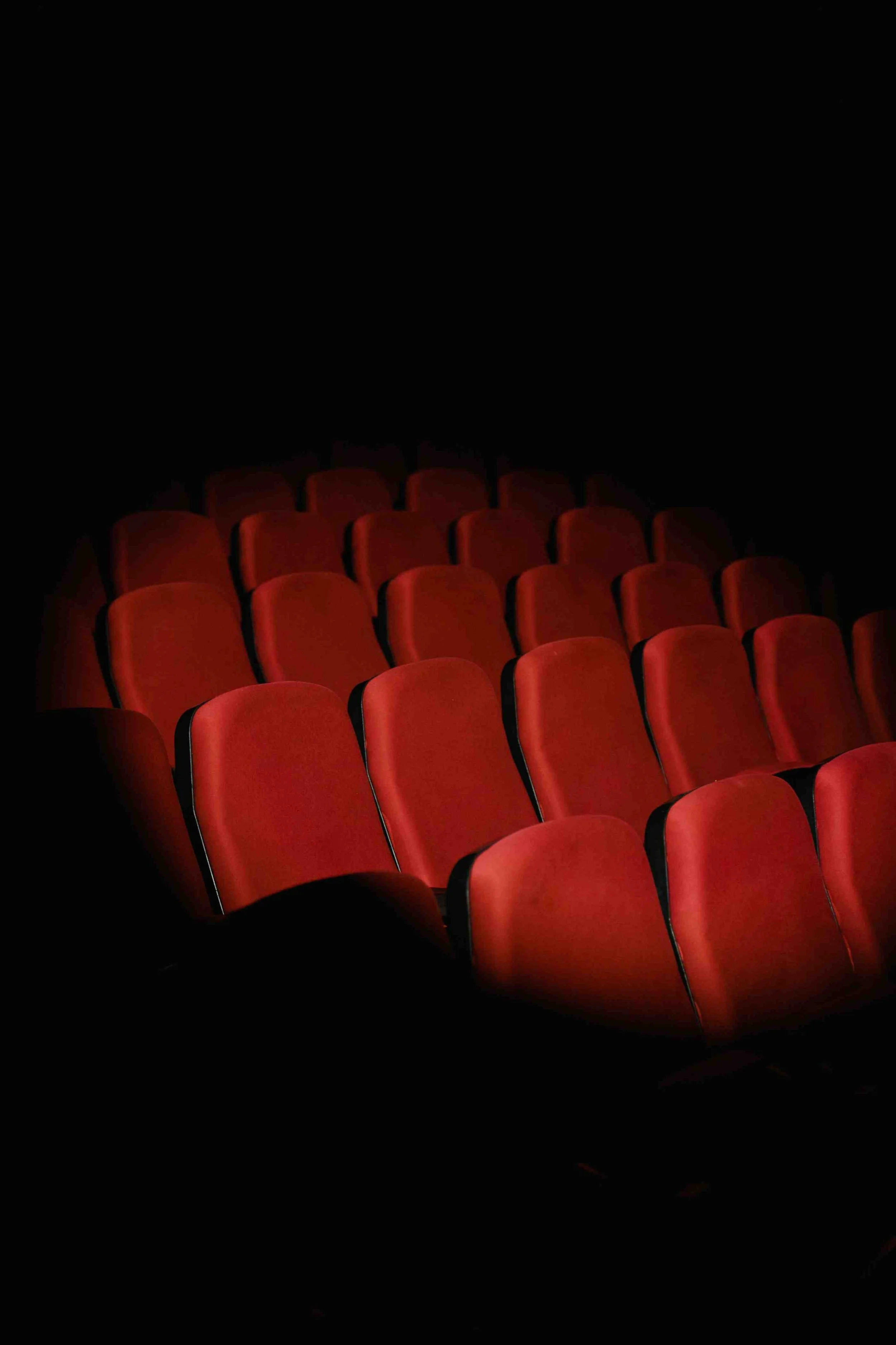 Empty red theater seats with black armrests in a dark theater.