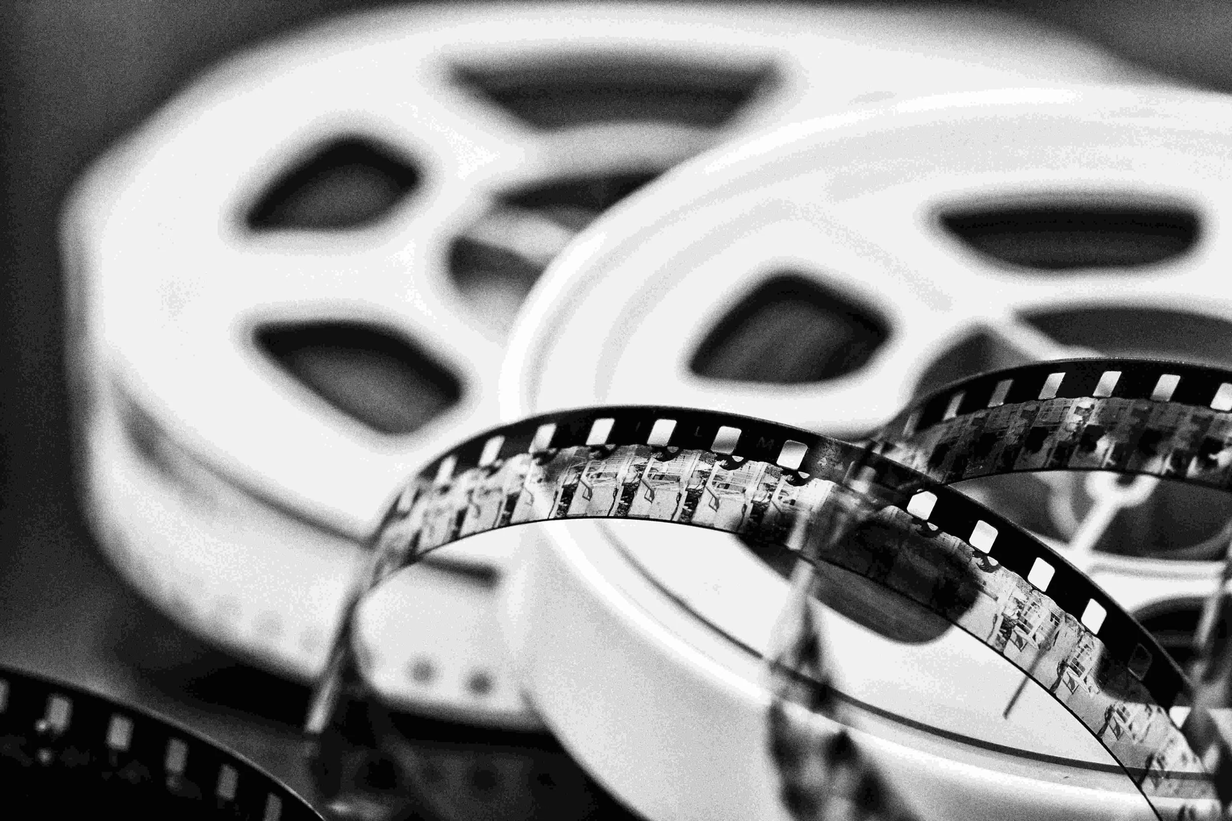 Close-up image of film reels in black and white, with the reels' perforations visible.