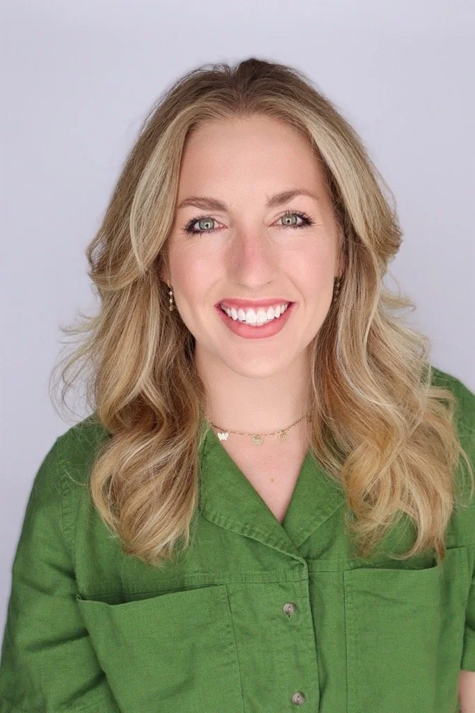 A woman with blonde hair, wearing a green button-up shirt and jewelry, smiling at the camera against a neutral background.