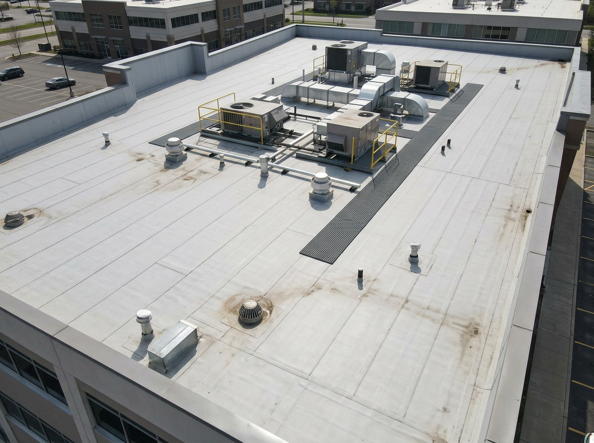 Close aerial view of a commercial flat roof with HVAC equipment, vents, seams, drains, and parapet edges
