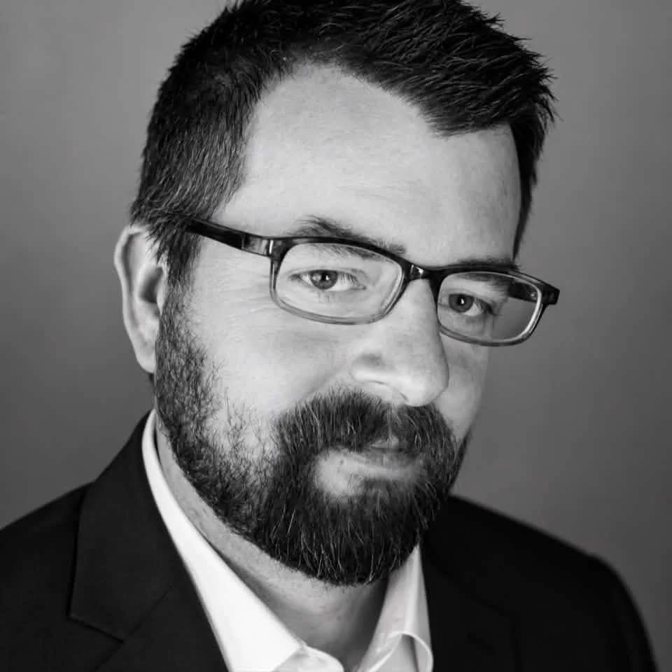 Black and white portrait of a man with glasses, a beard, and a mustache wearing a suit and white shirt.
