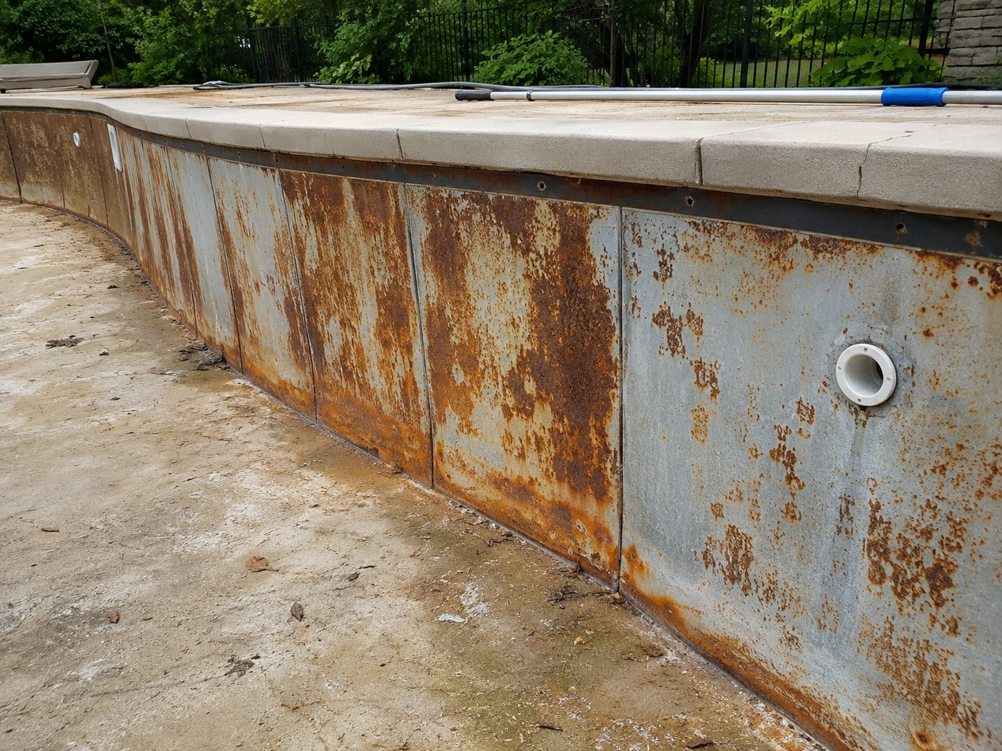 Close-up of a rusted metal pool wall with a drain pipe and a pool skimmer on top.
