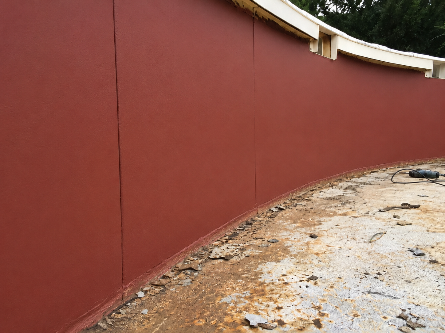 A curved red wall under construction with shingled ground and construction tools on the floor.