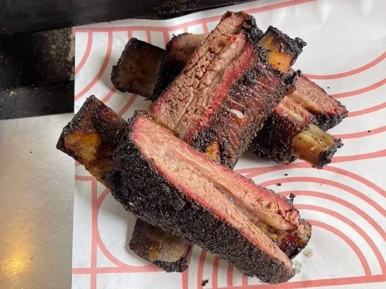 Close-up of smoked beef ribs with a dark, smoky crust, showing pink smoke ring and tender meat inside.