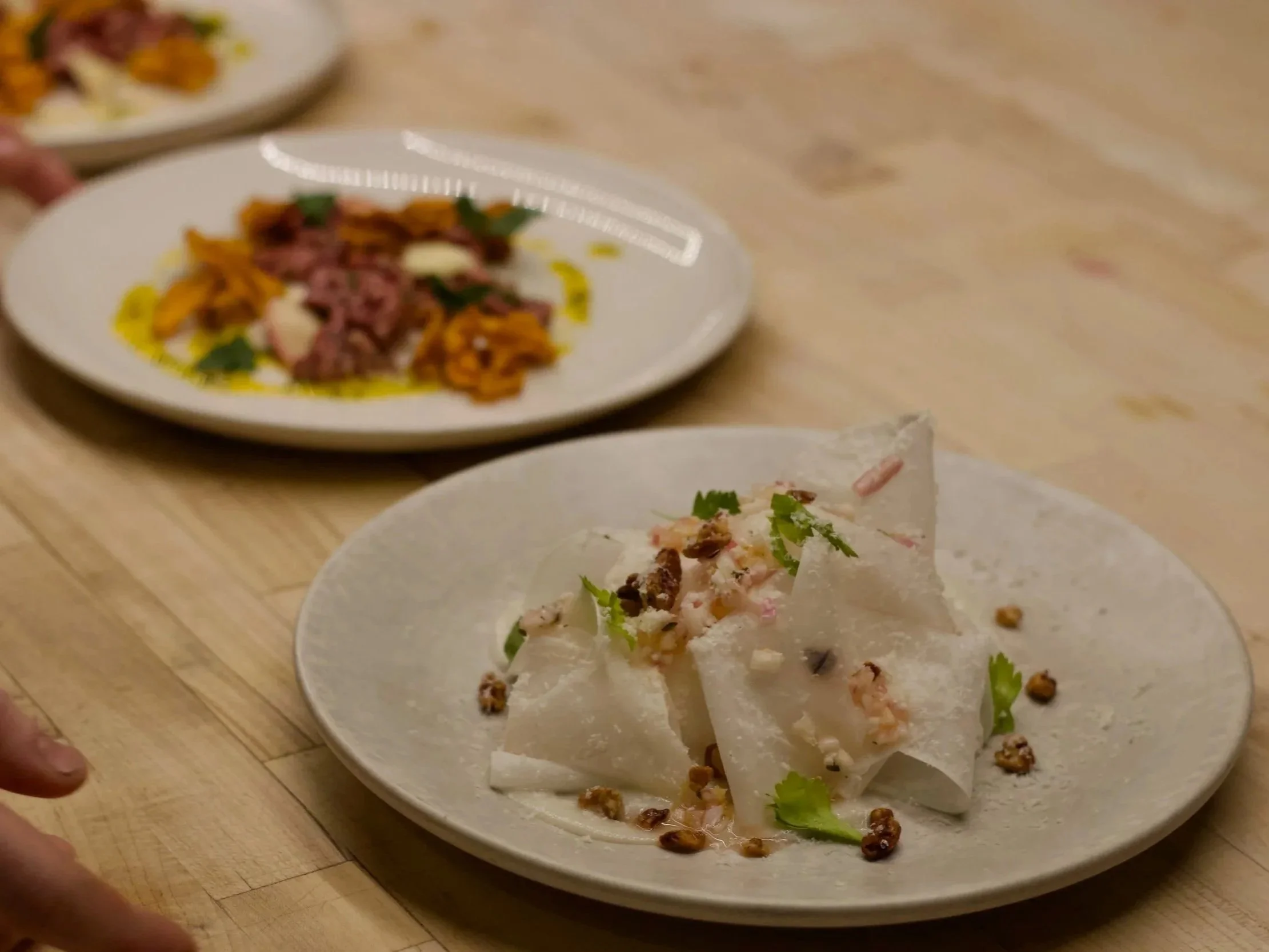 Close-up photo of a plate with tacos garnished with cilantro and scattered black beans, on a wooden table with other plates of food visible in the background.