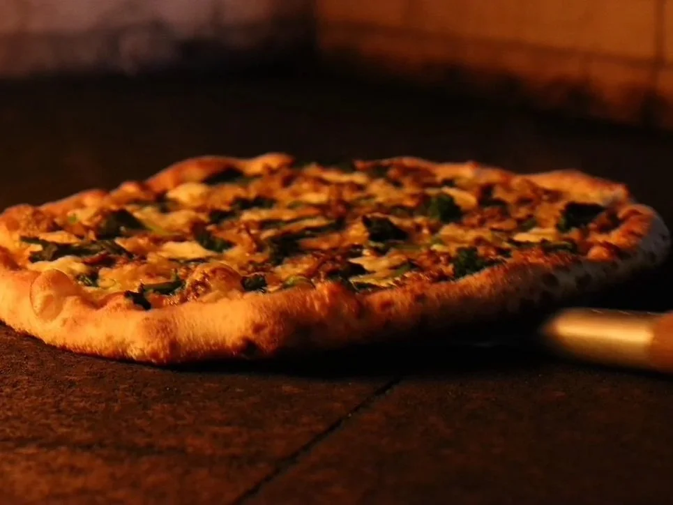 Pizza with cheese, green peppers, and mushrooms baking in a wood-fired oven.