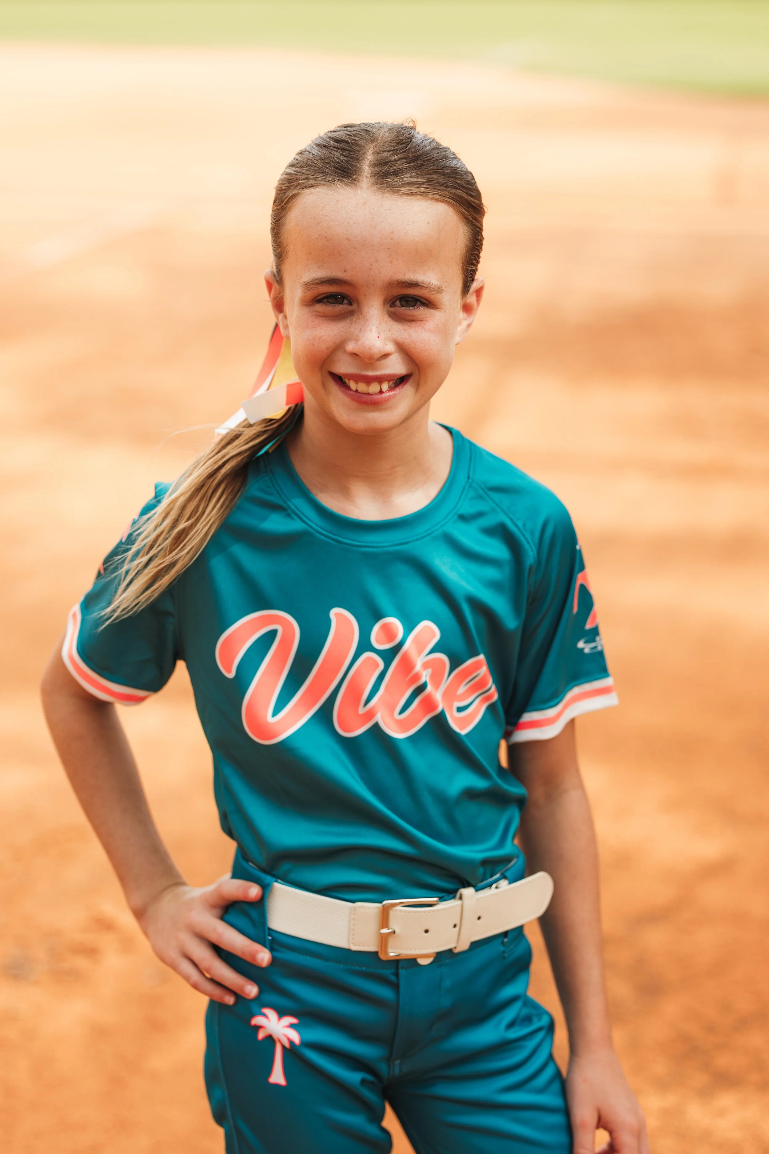 Lucy, Vibe softball player number 4, smiles for a portrait in her teal uniform on the field.