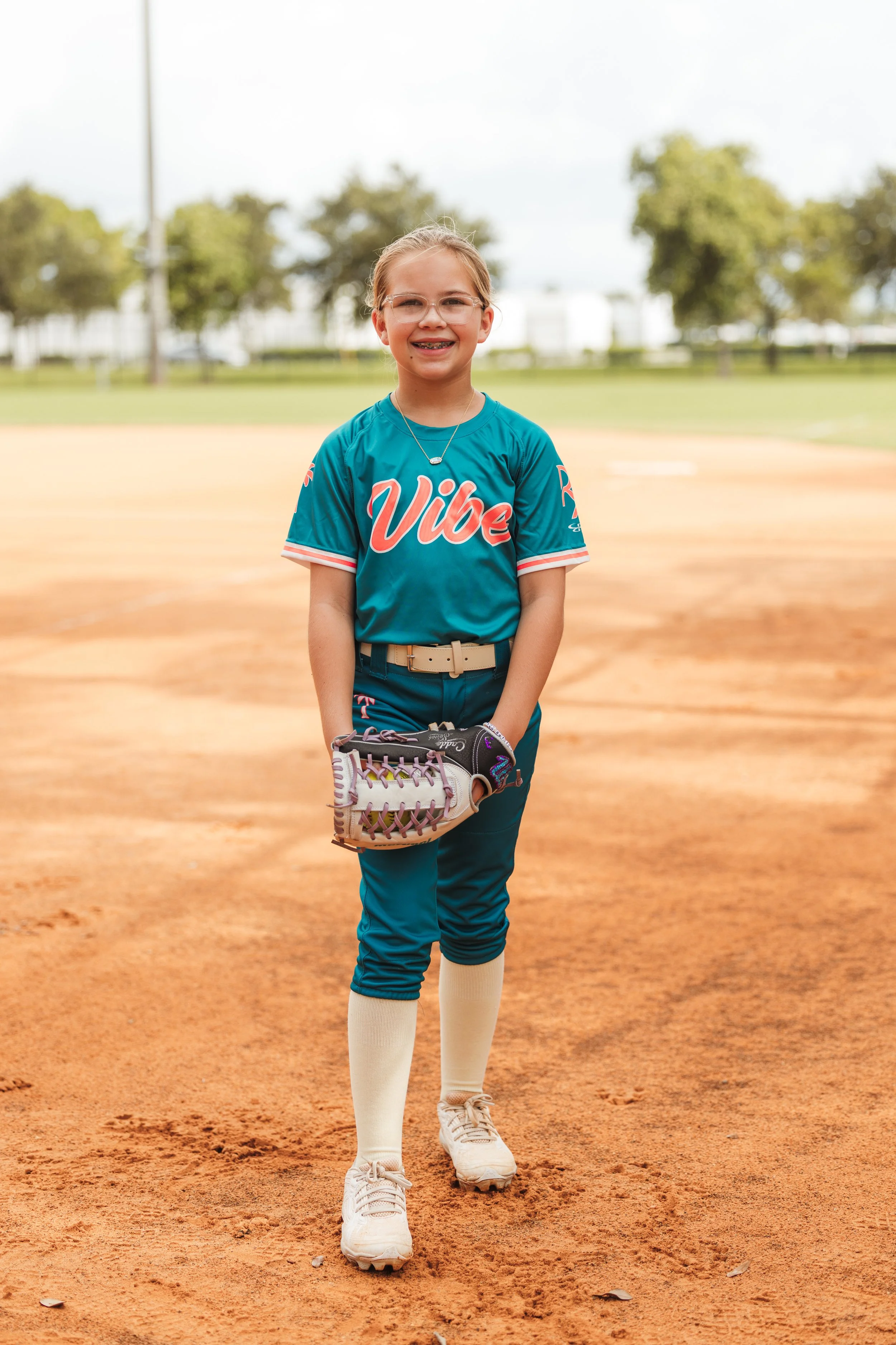 Harper, Vibe softball player number 3, smiles on the infield while holding a softball and glove.