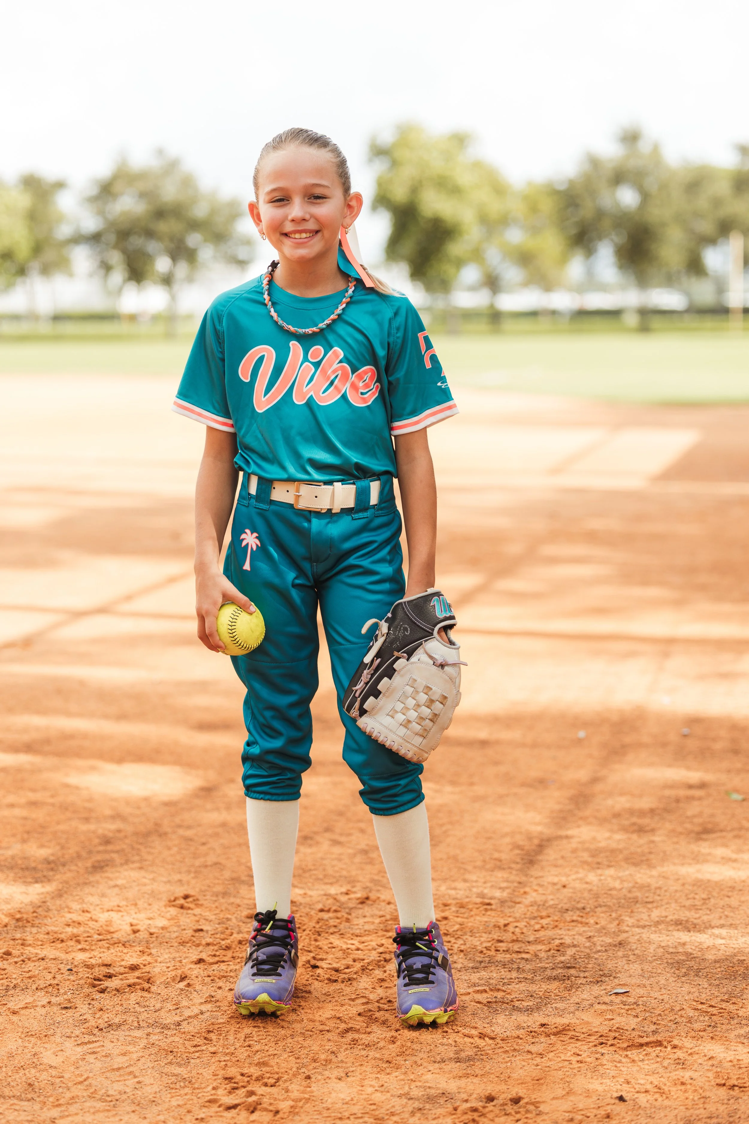 Shawn, Vibe softball player number 24, smiles on the infield while holding a softball and glove.