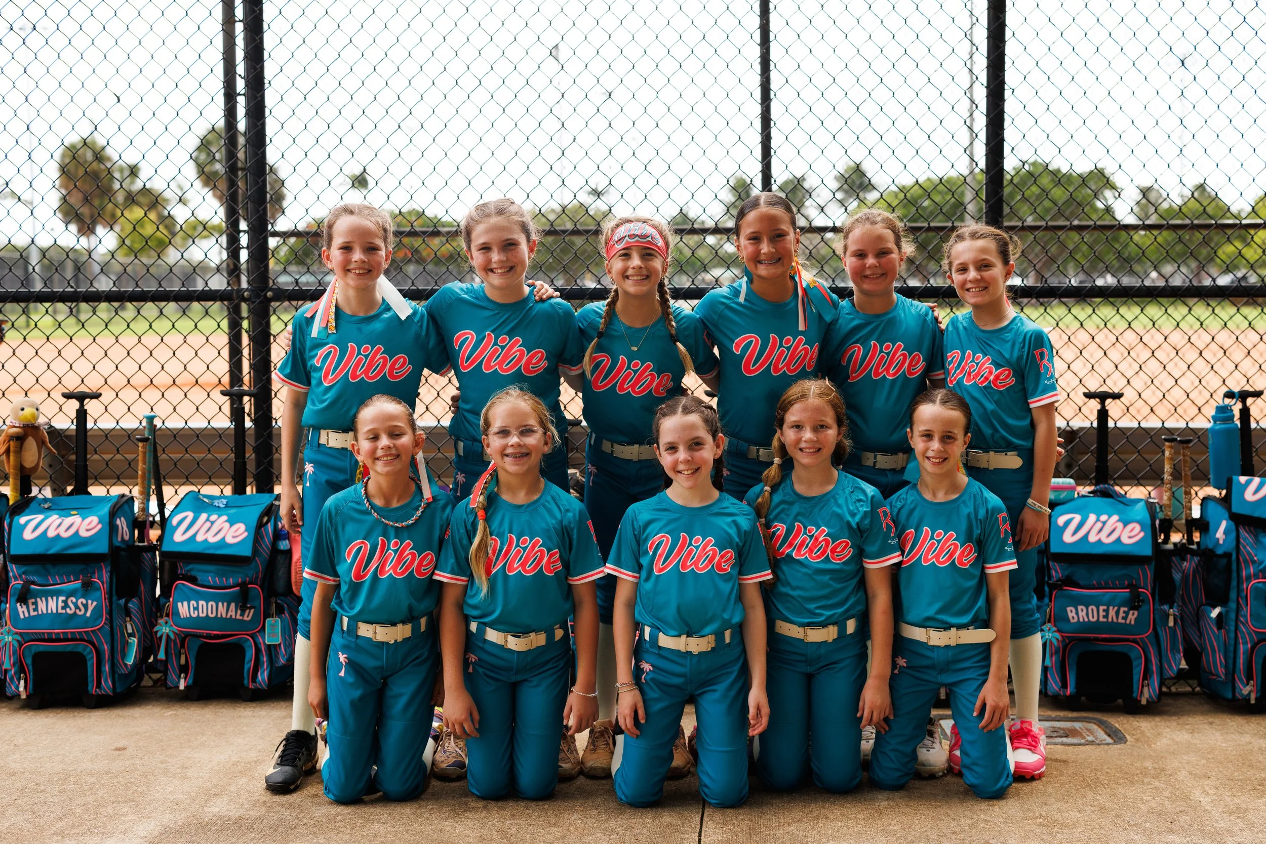Eleven smiling youth softball players in teal Vibe uniforms pose in two rows beside their equipment bags.